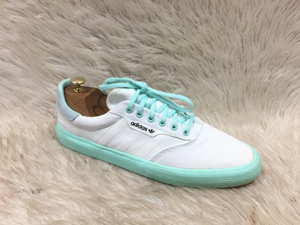 White Adidas sneaker with turquoise accents on a fur surface