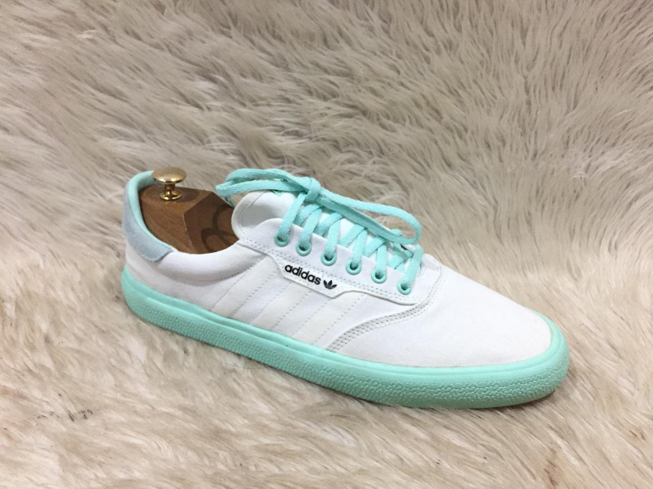 White Adidas sneaker with turquoise accents on a fur surface